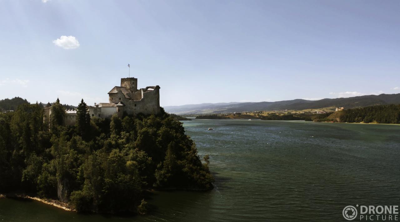 Panorama jeziora Czorsztyńskiego z zamkiem w Niedzicy sfotografowanym z drona w słoneczny dzień.