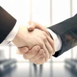 Uścisk dłoni dwóch osób w garniturach, symbolizujący zawarcie umowy kredytowej, z widocznymi detalami mankietów i delikatnym rozmyciem tła biurowego.