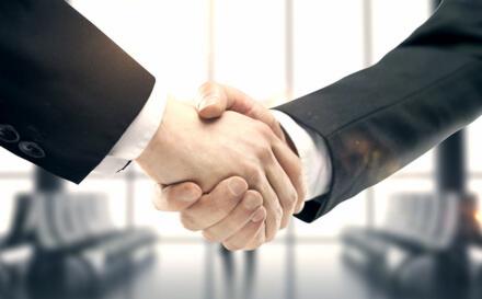 Uścisk dłoni dwóch osób w garniturach, symbolizujący zawarcie umowy kredytowej, z widocznymi detalami mankietów i delikatnym rozmyciem tła biurowego.