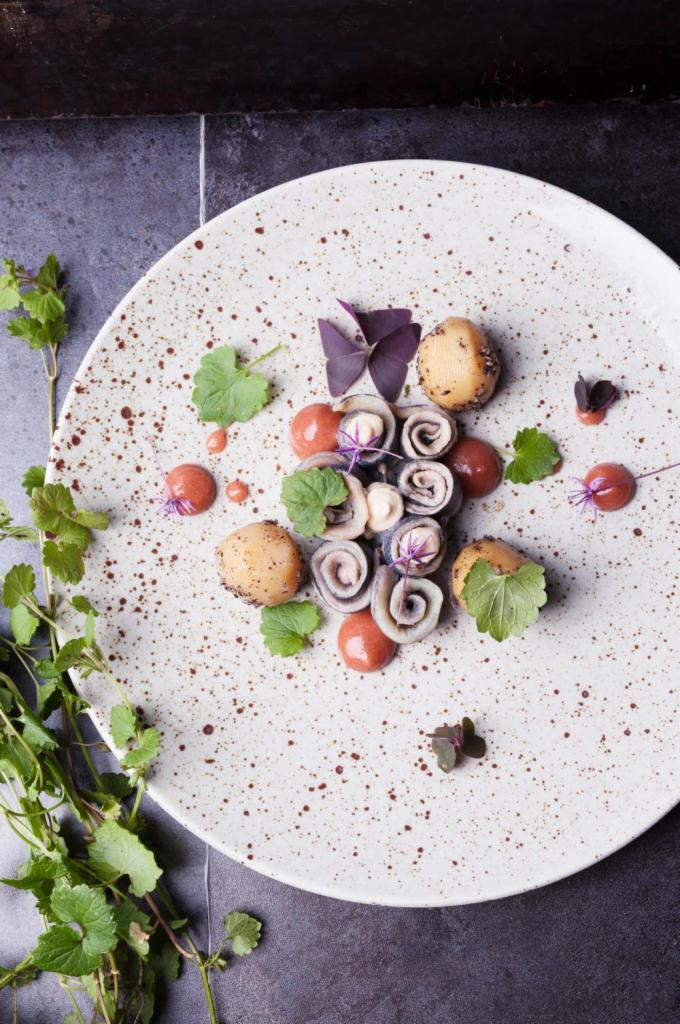 Elegancko podane danie na talerzu w stylu rustykalnym: roladki z ryby, ziemniaki, sos, jadalne kwiaty i świeże zioła.