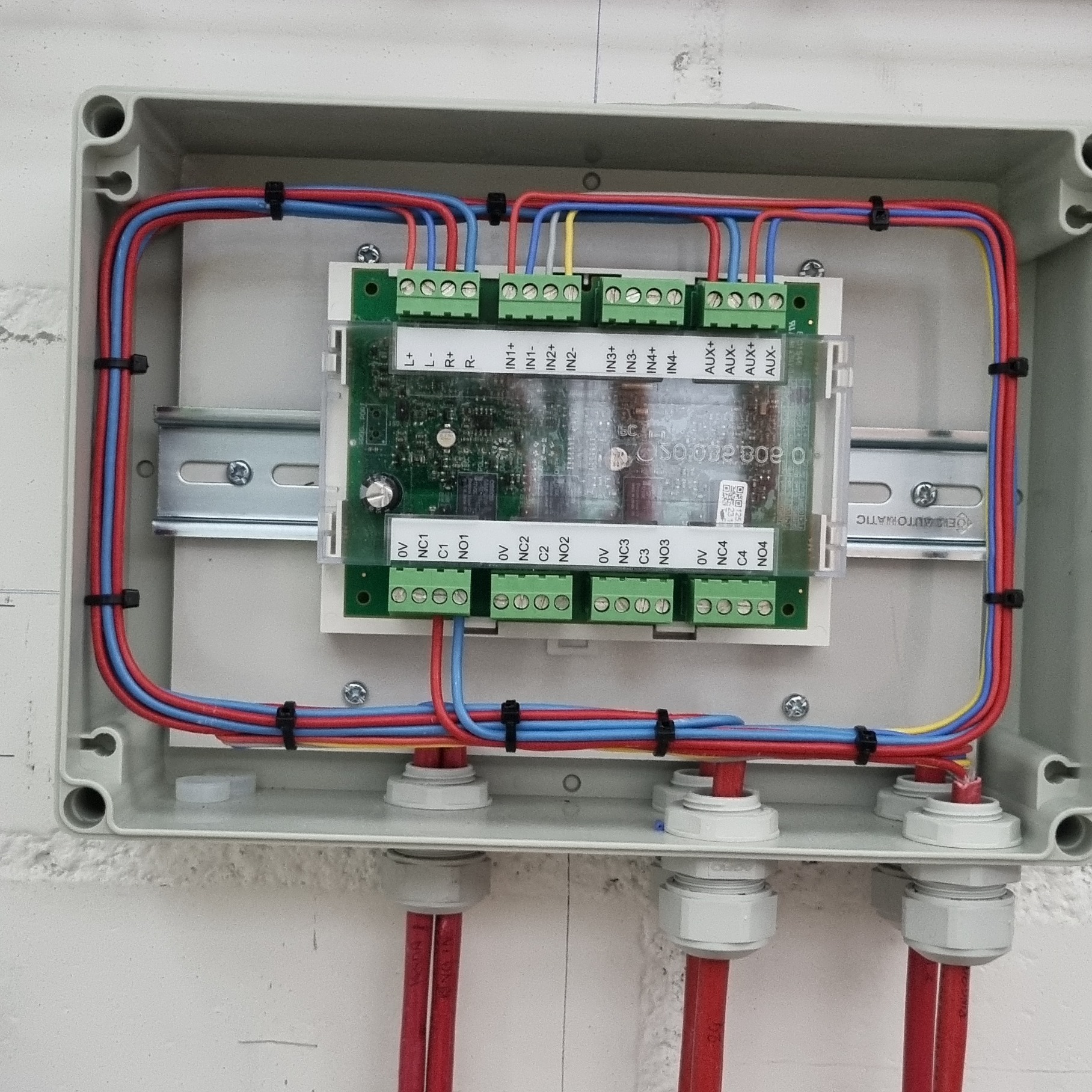 Rozdzielnica elektryczna z podłączonymi przewodami w kolorach niebieskim, czerwonym i żółtym, zabezpieczonymi czarnymi opaskami zaciskowymi, zamontowana na ścianie.