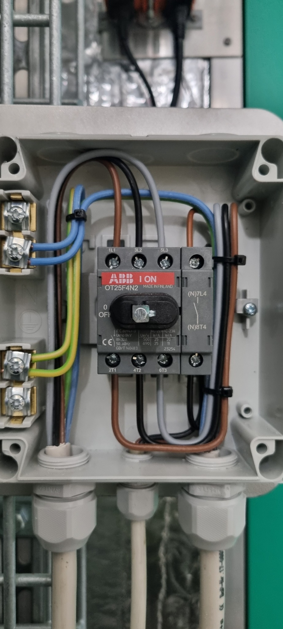 Rozdzielnica elektryczna z widocznymi przewodami, wyłącznikiem ABB OT25F4N2 i listwami zaciskowymi w szarej obudowie.