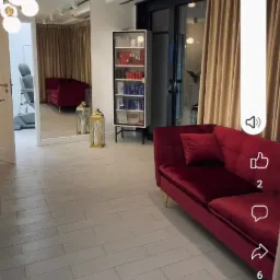 Wnętrze salonu kosmetycznego z bordową sofą, regałem z kosmetykami i lustrem odbijającym fotel zabiegowy.