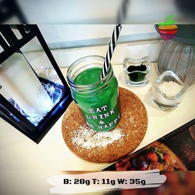 Zielony koktajl w słoiku z napisem 'Eat Drink & Be Happy' na korkowej podkładce, obok szklane naczynia z zielonym proszkiem i białymi kryształkami, w tle dekoracyjna dynia i lampion z lampkami.