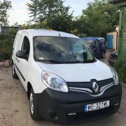 Biały samochód dostawczy Renault Kangoo z polską tablicą rejestracyjną WE 321WL, zaparkowany na żwirowym podłożu, z widocznym ogrodem w tle.