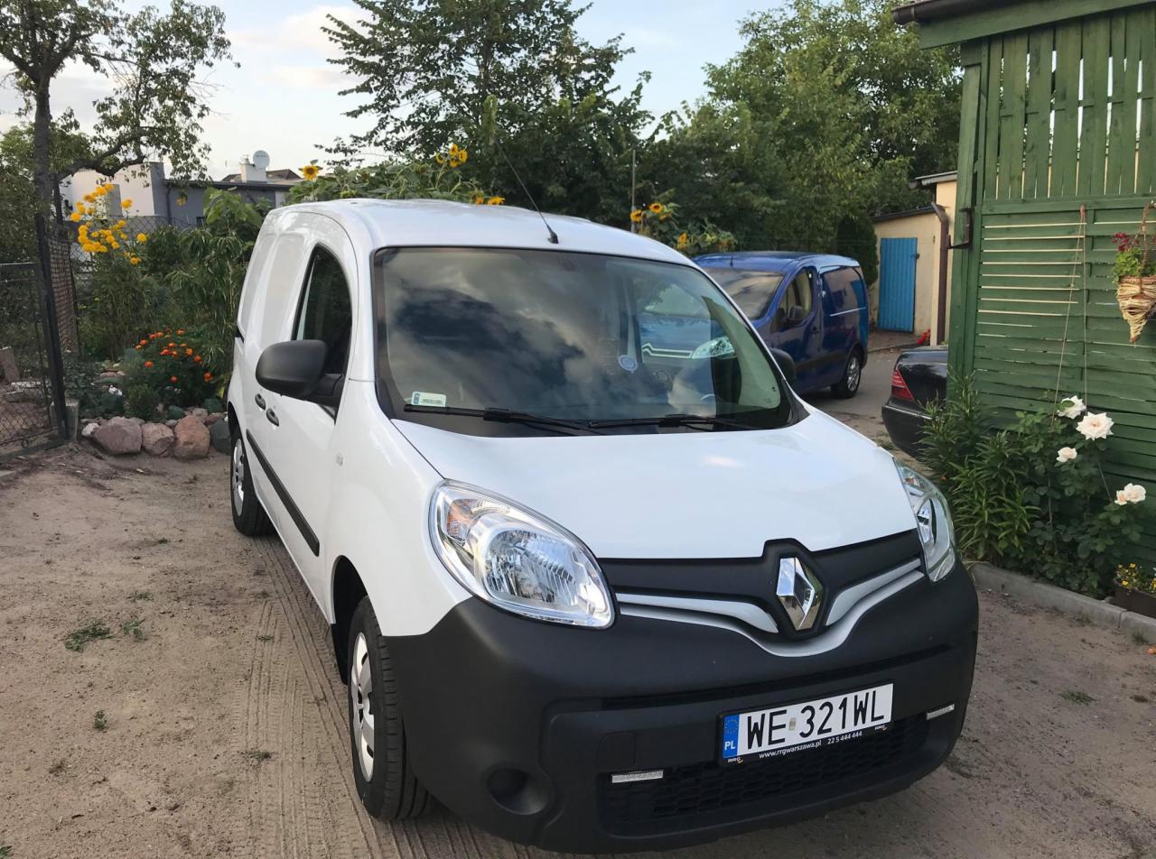 Biały samochód dostawczy Renault Kangoo z polską tablicą rejestracyjną WE 321WL, zaparkowany na żwirowym podłożu, z widocznym ogrodem w tle.