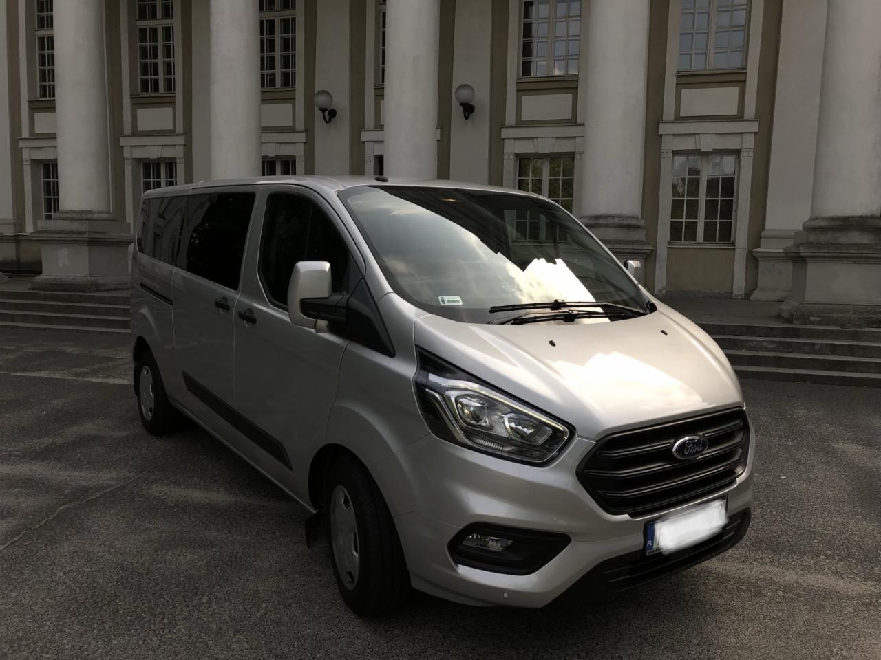 Srebrny Ford Transit Custom, zaparkowany na tle klasycystycznego budynku z kolumnami