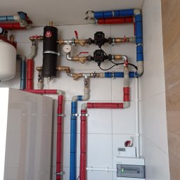 HCM-AirControl - Instalacja grzewcza z rurami w kolorze czerwonym i niebieskim, zaworami, pompami obiegowymi i zbiornikiem wyrównawczym w kotłowni w Skierniewicach, widoczny również panel sterowania.