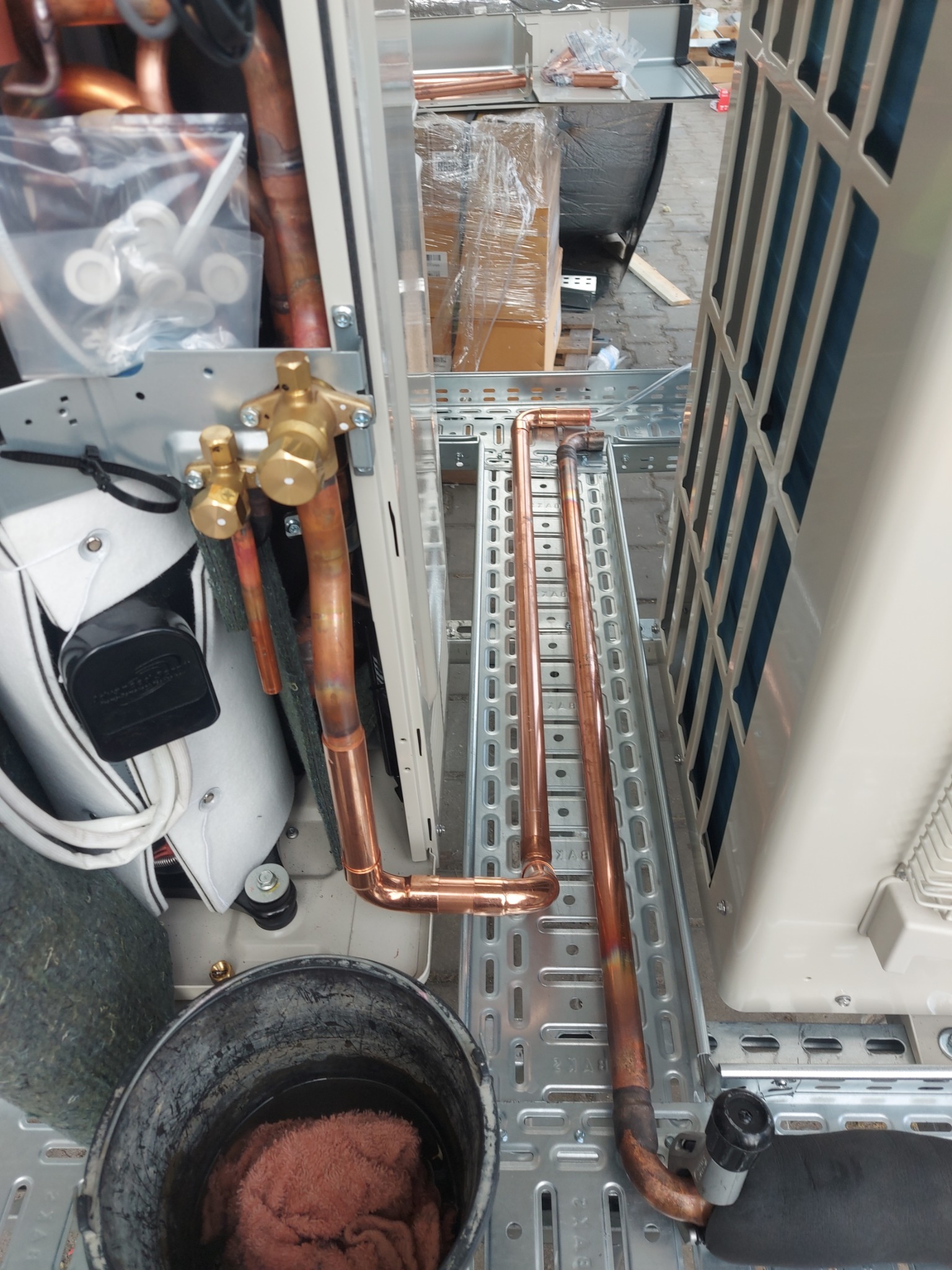 Montaż instalacji chłodniczej: miedziane rury łączone lutem twardym, widoczne zawory i elementy mocujące na metalowej konstrukcji wsporczej.