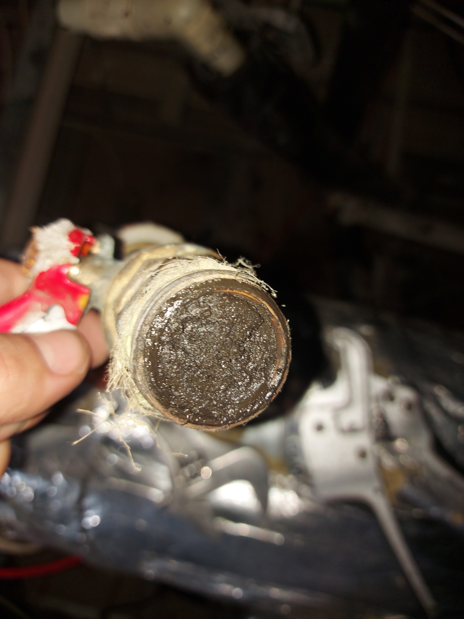 Zanieczyszczona końcówka rury hydraulicznej z pozostałościami uszczelniacza, trzymana w dłoni, widoczne narzędzia w tle.