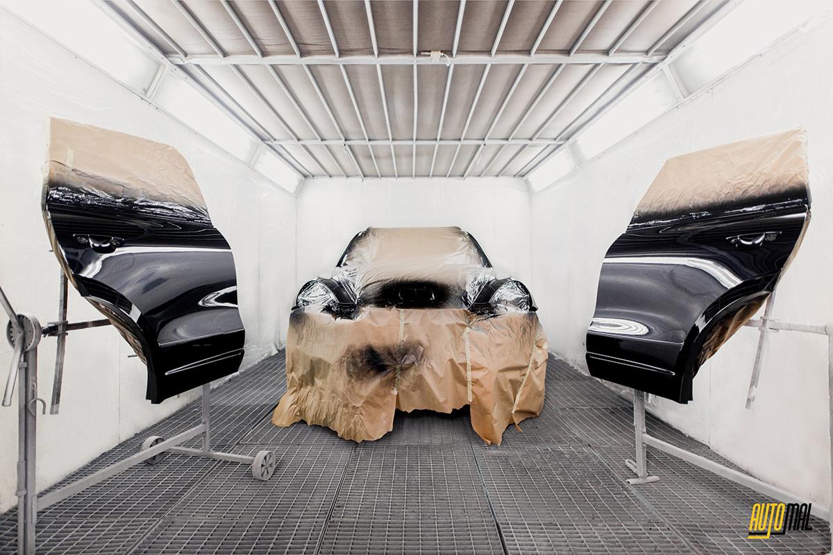 Samochód i dwie drzwi, osłonięte papierem malarskim, przygotowywane do lakierowania w kabinie lakierniczej z metalową kratą podłogową i oświetleniem sufitowym.