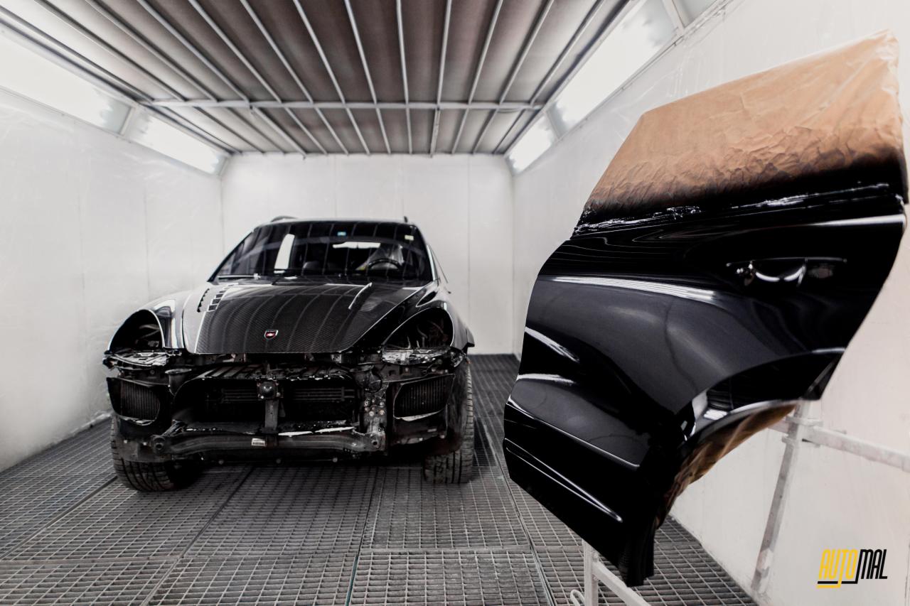 Częściowo rozebrany, czarny samochód w kabinie lakierniczej, z odnowionymi drzwiami w pierwszym planie, z widocznym logo firmy.