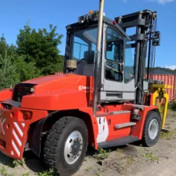 Czerwono-szary wózek widłowy kontenerowy marki Kalmar, widoczny z boku na tle zieleni i błękitnego nieba.
