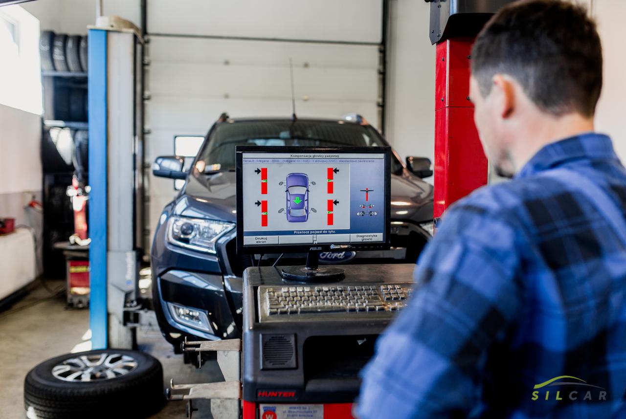 Mężczyzna w warsztacie samochodowym sprawdza geometrię kół ciemnego Forda Rangera na urządzeniu Hunter z widocznym interfejsem diagnostycznym na ekranie.