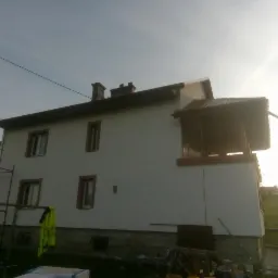 Dwupiętrowy dom po tynkowaniu elewacji, z widocznymi rusztowaniami i elementami wykończeniowymi balkonu.