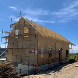 Budowa domu w Chełmcu na etapie montażu konstrukcji szkieletowej z płyt OSB i więźby dachowej, widoczne rusztowania i składowane deski.