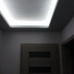 Nowoczesny sufit podwieszany z oświetleniem LED w korytarzu, widoczna drewniana drzwi z przeszkleniami.