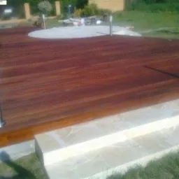 Drewniany taras z egzotycznego drewna, oświetlony niskimi lampami, z marmurowymi schodami prowadzącymi do ogrodu.