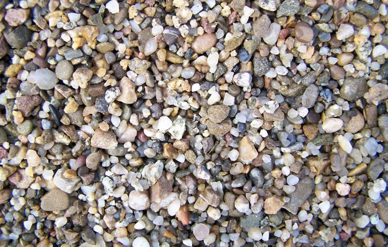 Makro zbliżenie na różnokolorowe, drobne kamyczki i żwir o gładkiej powierzchni, niektóre z widocznymi białymi żyłkami kwarcu.