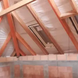 Konstrukcja drewniana dachu z oknami połaciowymi, ocieplona od wewnątrz, widok na mur z cegły dziurawki w surowym stanie.