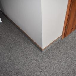 wall & floor solution - Szara wykładzina dywanowa w rogu pokoju, przy białej ścianie i drewnianej ościeżnicy drzwiowej.