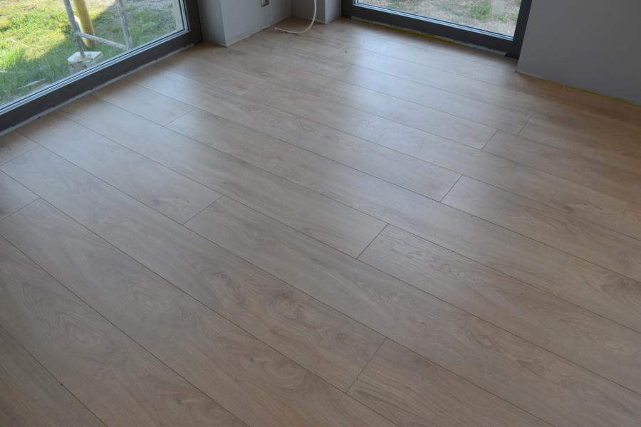 Jasne panele podłogowe ułożone w nowym pomieszczeniu z dużym oknem, widok ukośny.