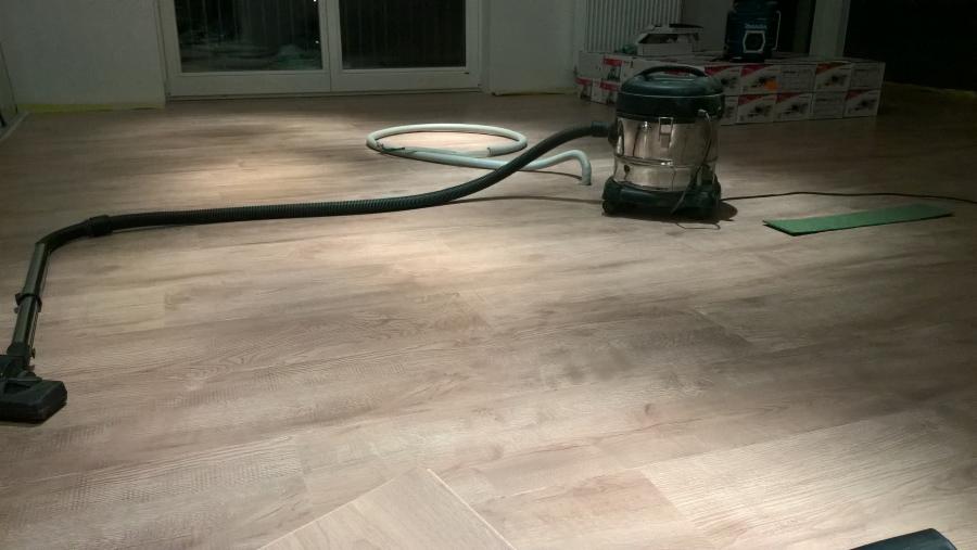 Świeżo ułożone panele podłogowe z widocznym odkurzaczem przemysłowym i resztkami zabrudzeń po montażu.