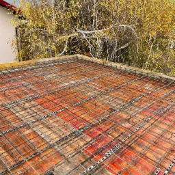 Siatka zbrojeniowa na deskowaniu stropu, z widocznymi dystansami, na tle jesiennego drzewa.