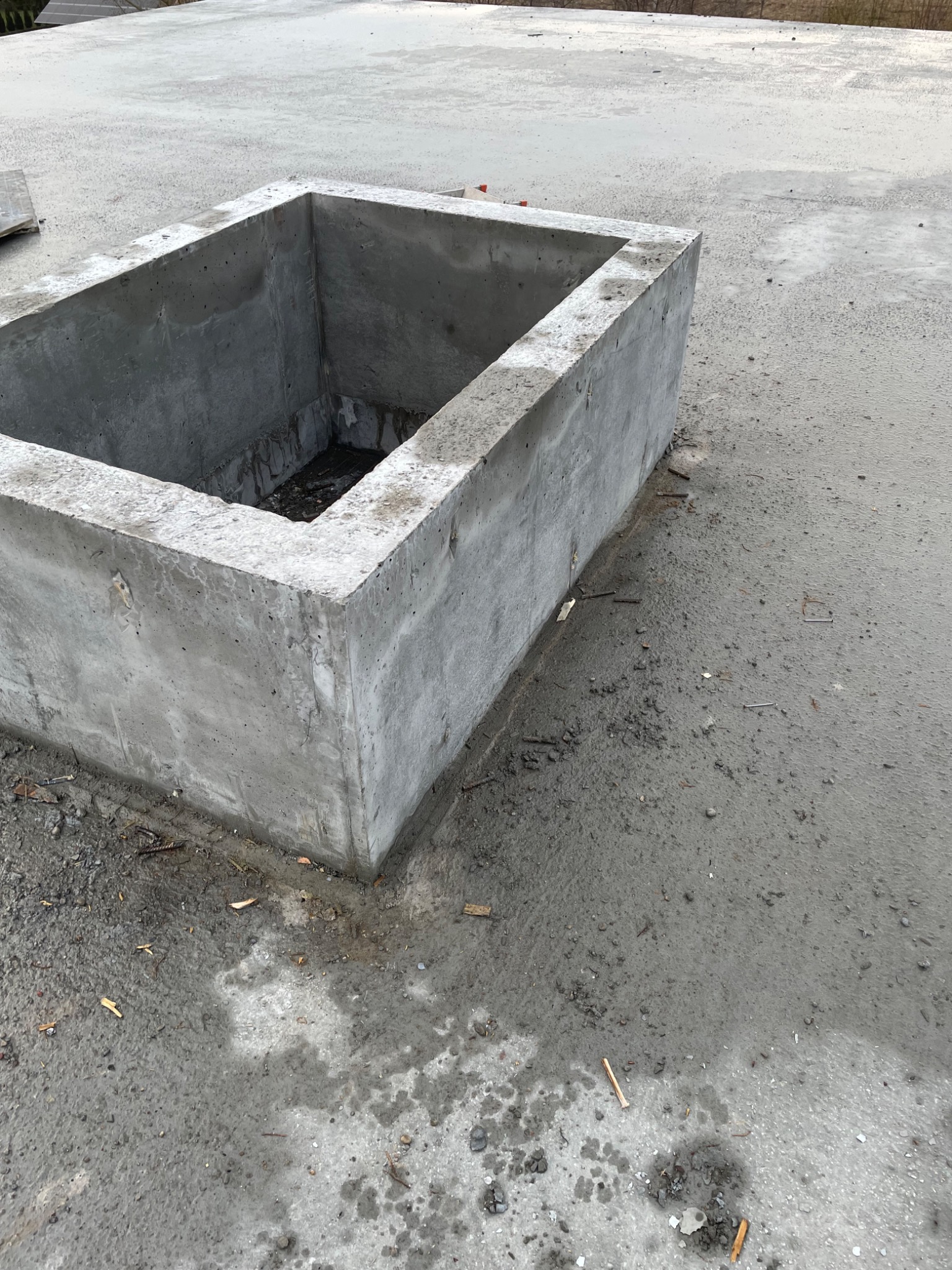 Surowy betonowy otwór w stropie, prawdopodobnie przygotowany pod instalacje, z widocznymi śladami po deskowaniu i drobnymi fragmentami gruzu wokół.