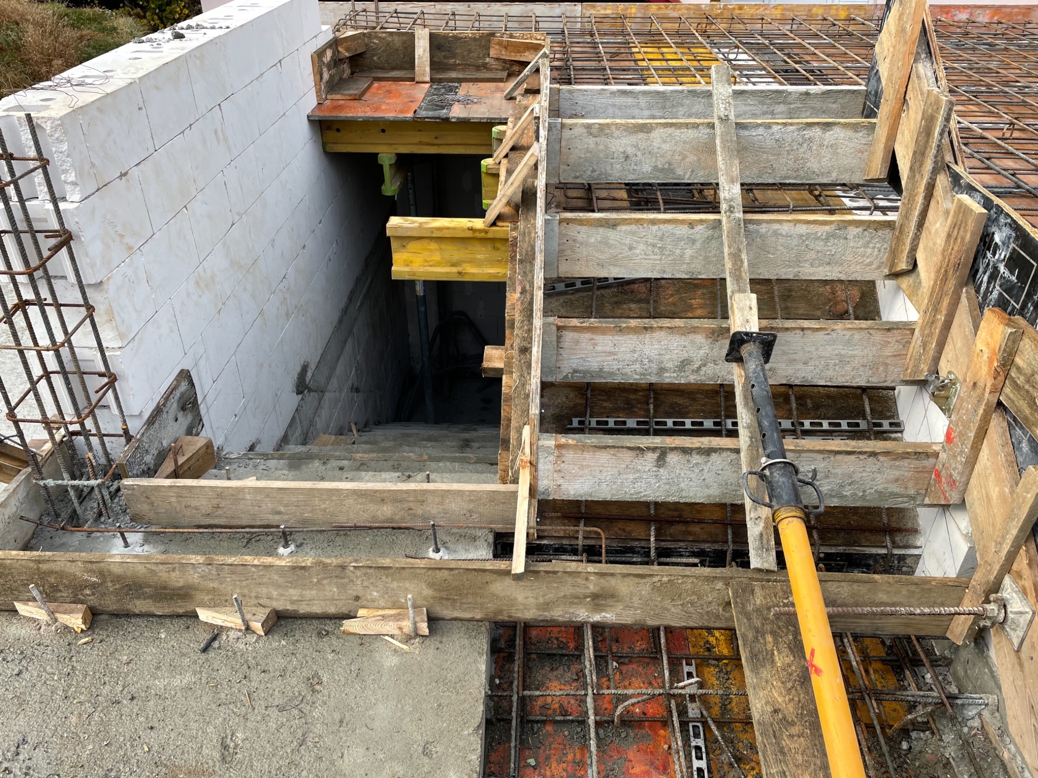 Konstrukcja schodów w trakcie betonowania, widoczne drewniane szalunki, zbrojenie oraz podpory teleskopowe.