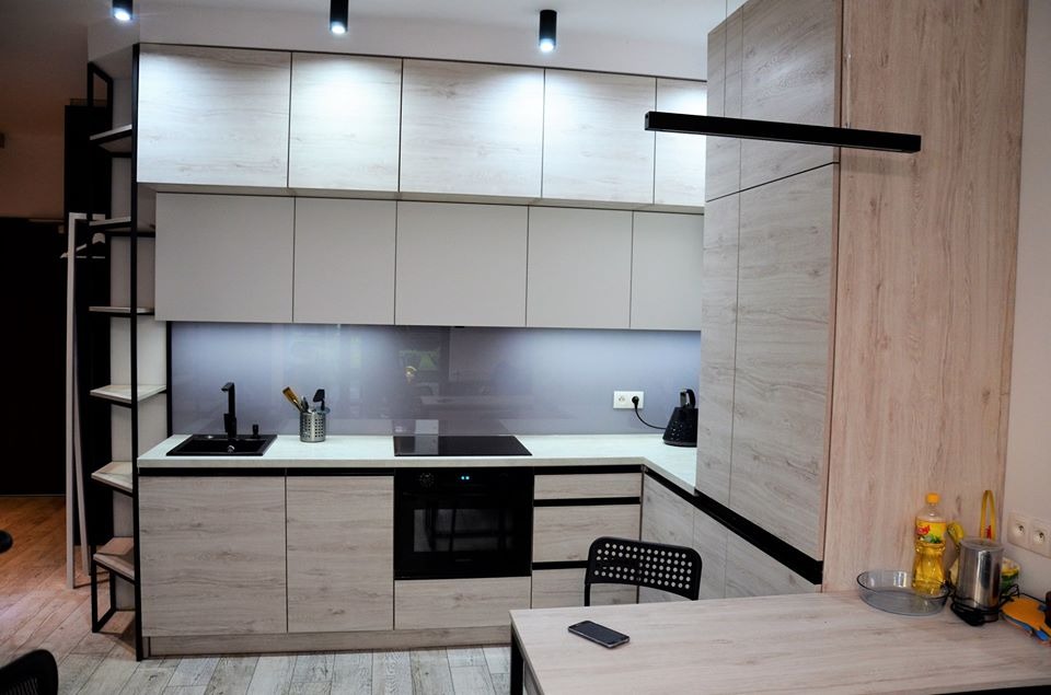 Nowoczesna kuchnia z białymi górnymi szafkami i drewnopodobnymi dolnymi, czarnymi akcentami, szklanym panelem nad blatem i minimalistycznym oświetleniem punktowym.