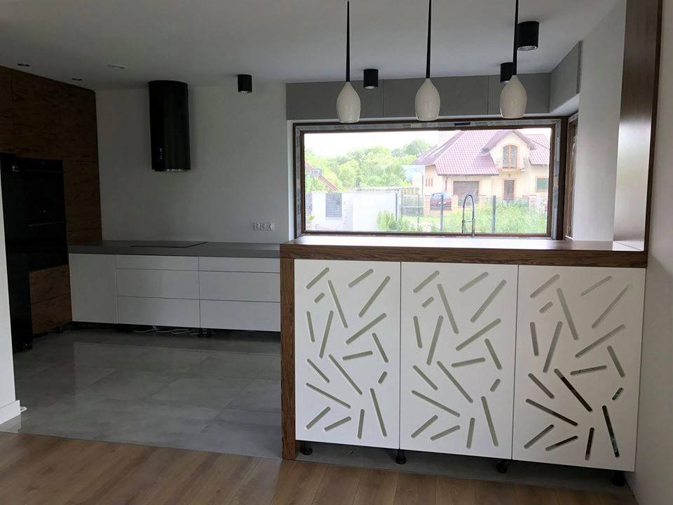 Nowoczesna kuchnia z białymi szafkami o geometrycznym wzorze, drewnianymi akcentami i oknem z widokiem na dom z czerwonym dachem.