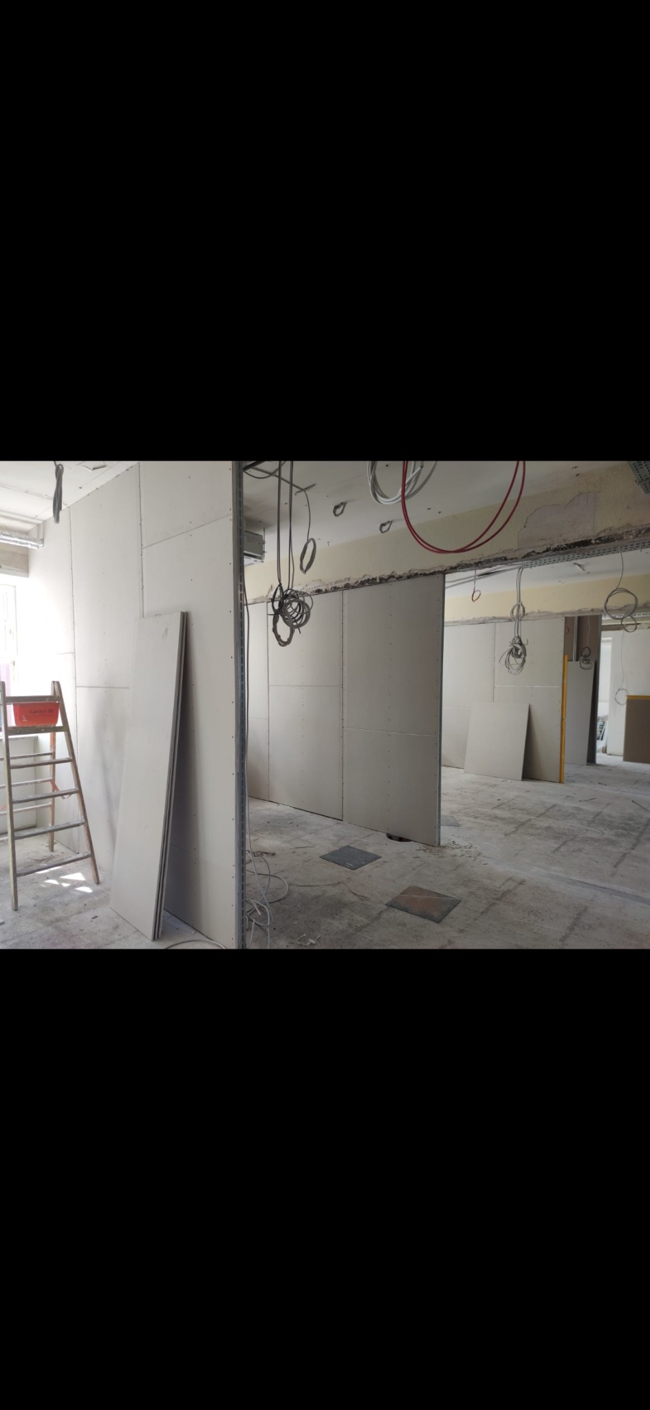 Wnętrze w trakcie montażu ścian działowych z płyt kartonowo-gipsowych; widoczne wiszące kable, drabina malarska i surowe podłoże.