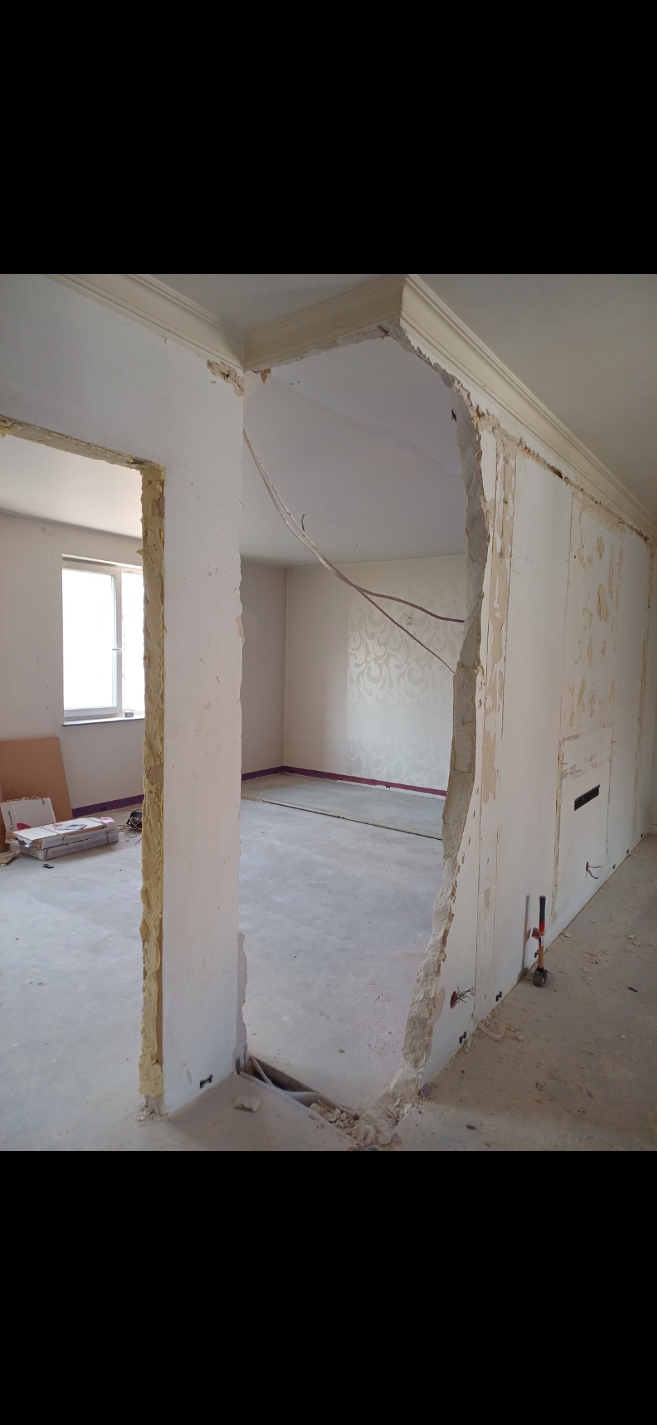 Demontaż ściany działowej w mieszkaniu, odsłonięte przewody elektryczne, widoczne fragmenty tapety na ścianie w tle.