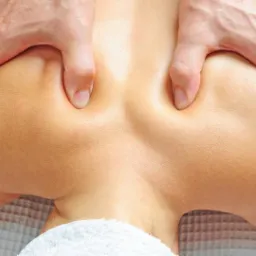 Masaż barków i górnej części pleców wykonywany dwiema dłońmi na białym ręczniku.