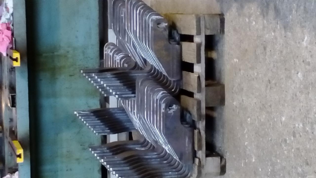 Stos metalowych elementów wyciętych z blachy, ułożonych na drewnianej palecie w warsztacie.