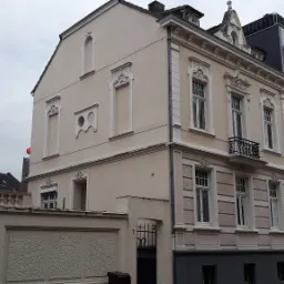 Odrestaurowana kamienica z elementami dekoracyjnymi fasady, widoczna z perspektywy ulicy, obok nowoczesny budynek.