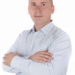 Portret mężczyzny w jasnoniebieskiej koszuli z założonymi rękami na białym tle.