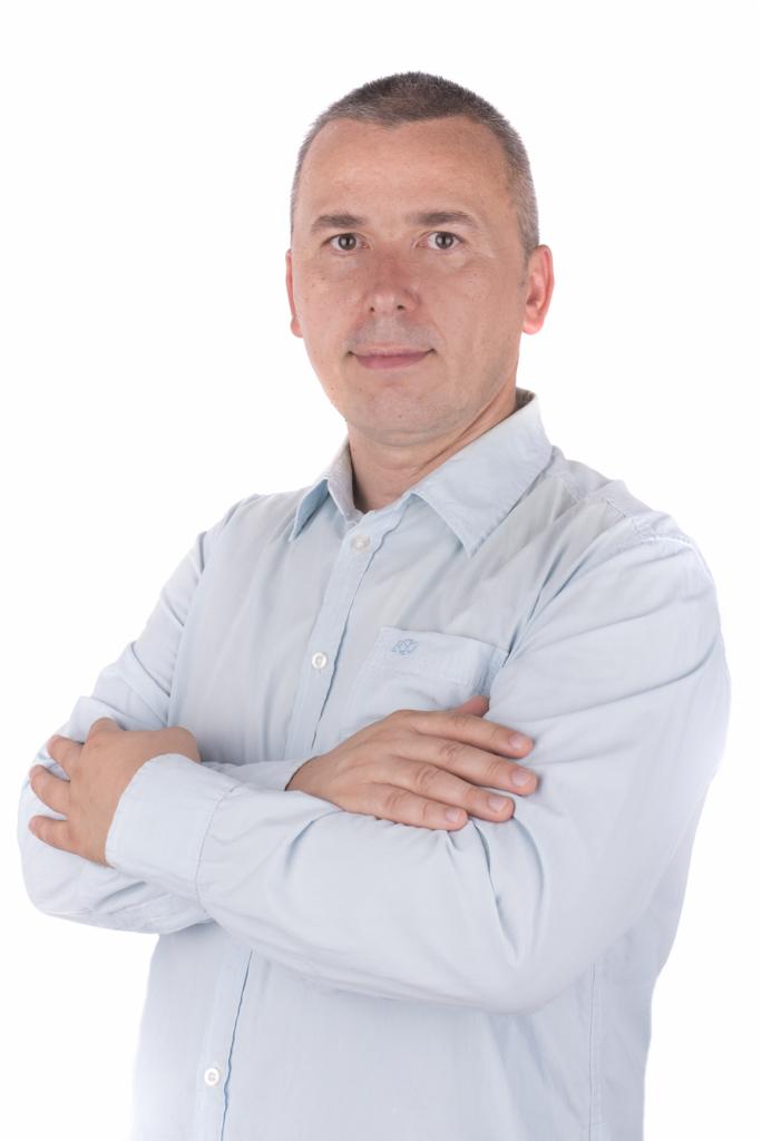 Portret mężczyzny w jasnoniebieskiej koszuli z założonymi rękami na białym tle.