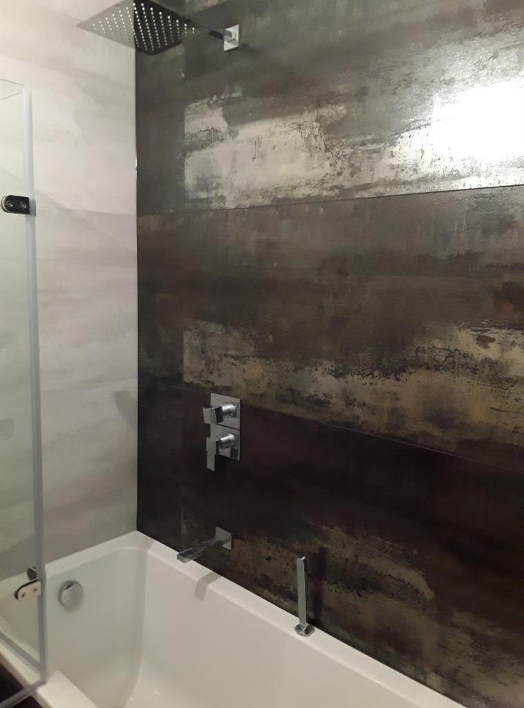 Nowoczesna łazienka w Krakowie z wanną, szklanym parawanem i panelami ściennymi imitującymi rdzę oraz deszczownicą.