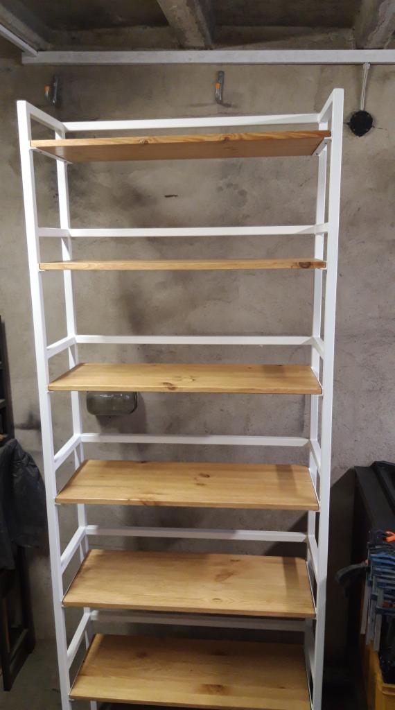Metalowy regał magazynowy z białym stelażem i drewnianymi półkami na tle szarej ściany w surowym wnętrzu.