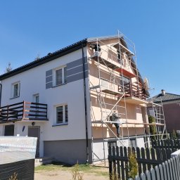 El-bud Paweł Dubicki - Dwukondygnacyjny dom w trakcie prac elewacyjnych, z widocznym rusztowaniem i pracownikiem wykonującym tynkowanie, częściowo ocieplony, z paczkami materiałów budowlanych przed budynkiem.