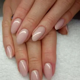 Dłonie z owalnymi paznokciami pokrytymi lakierem w odcieniu pudrowego różu z delikatnym połyskiem, na tle białego ręcznika.