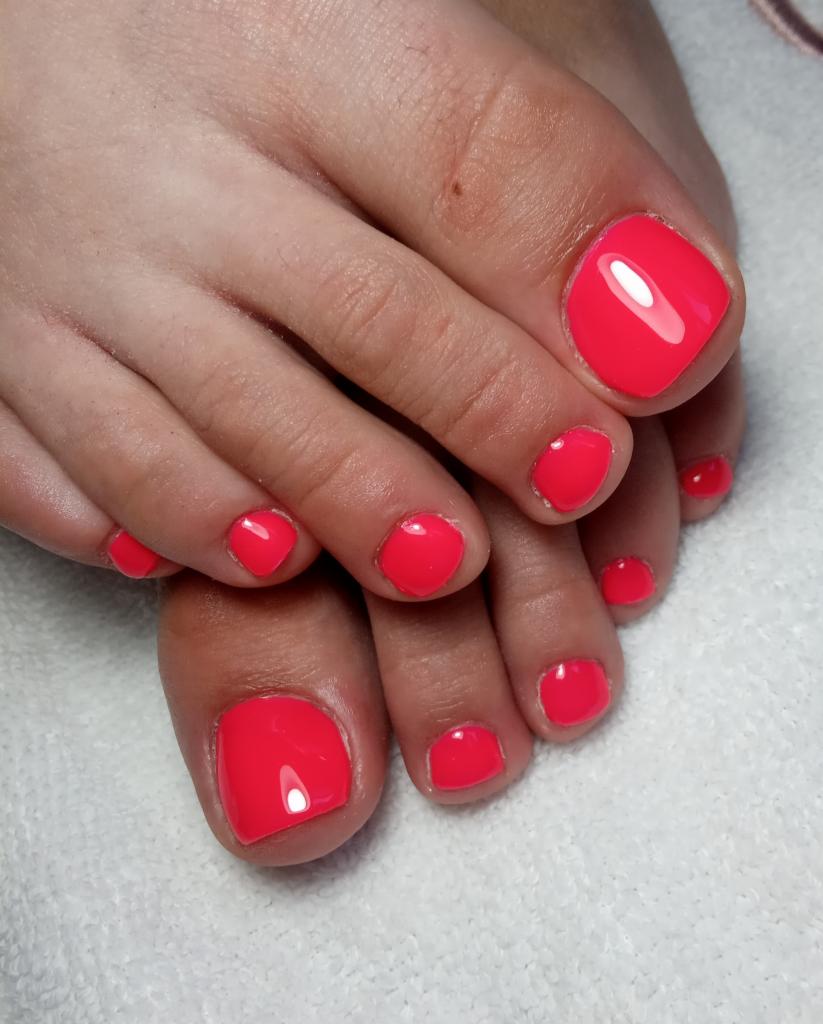 Pomalowane na jaskrawy koralowy kolor paznokcie u stóp, widoczne z bliska na tle białego ręcznika.