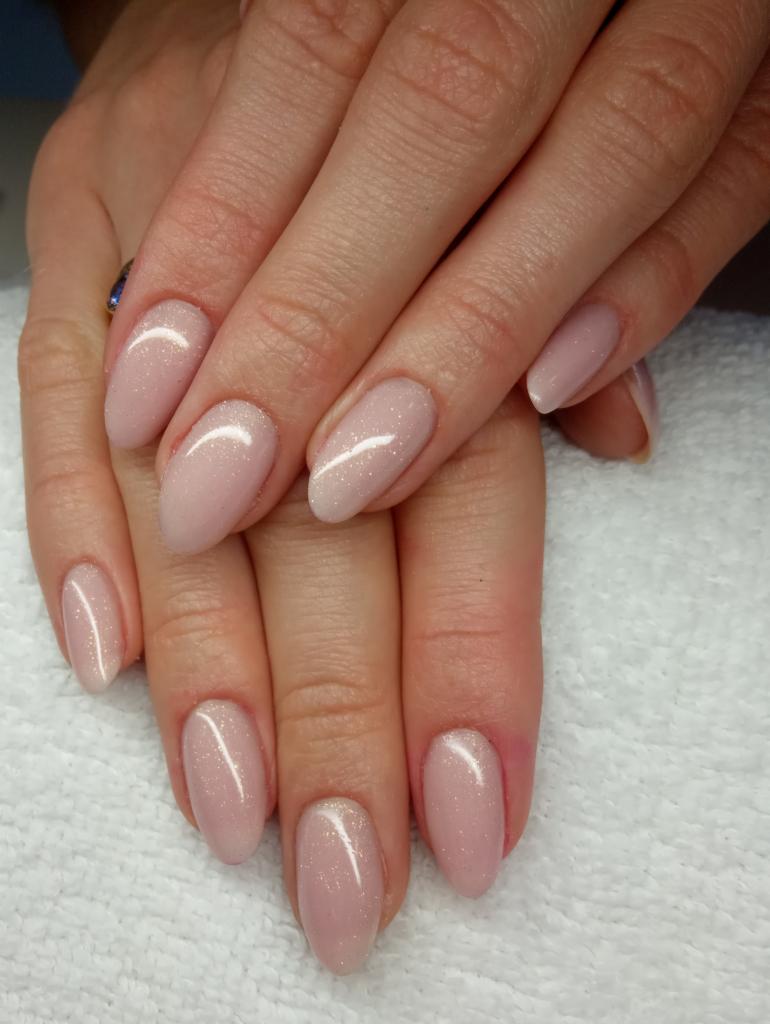 Dłonie z owalnymi paznokciami pokrytymi lakierem w odcieniu pudrowego różu z delikatnym połyskiem, na tle białego ręcznika.