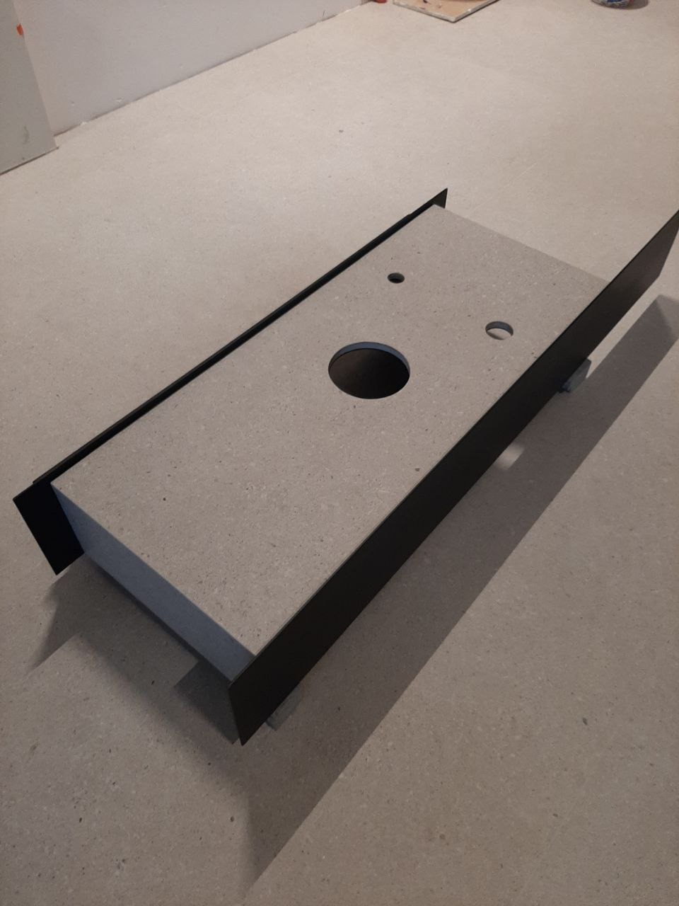 Blat pod umywalkę z otworami, w trakcie montażu, surowy beton i czarne obramowanie.