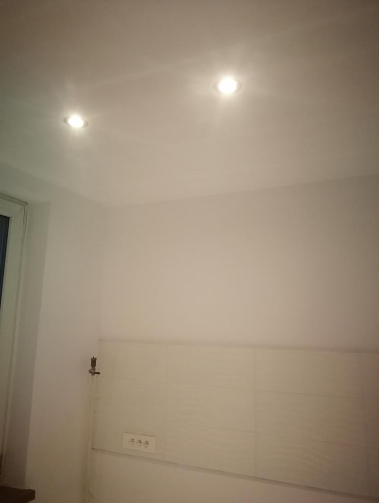 Świeżo pomalowane, białe ściany z zamontowanymi punktowymi lampami sufitowymi w mieszkaniu w Bytomiu, widoczne płytki na ścianie i gniazdka elektryczne.