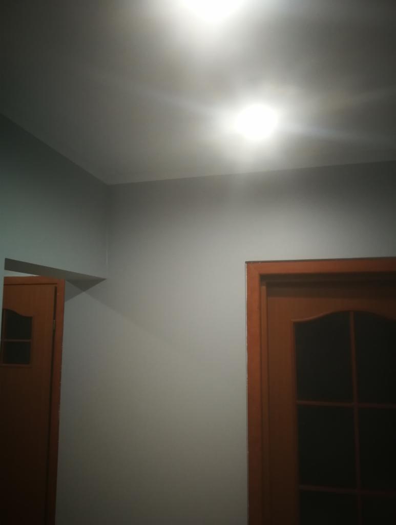 Pomieszczenie po malowaniu ścian na szaro, widoczne dwie drewniane ościeżnice drzwiowe, oświetlenie sufitowe.