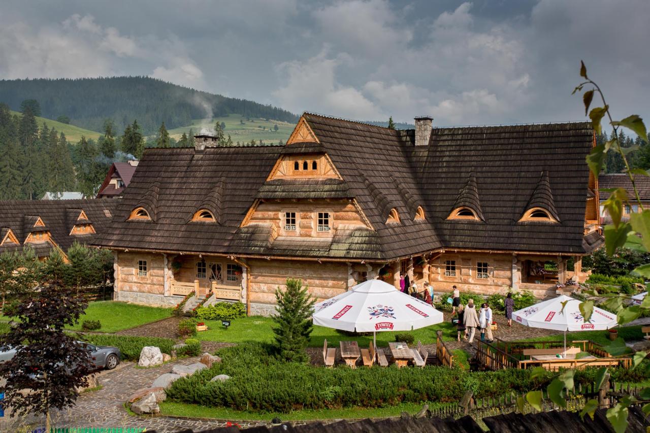 Tradycyjny, drewniany hotel górski z charakterystycznym dachem, otoczony zielenią, z parasolami i stolikami dla gości na zewnątrz.