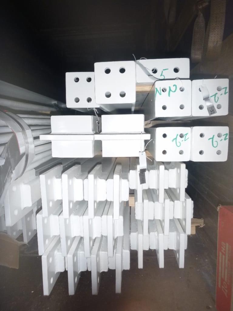 Białe, pomalowane elementy stalowe, prawdopodobnie łączniki i wsporniki, ułożone w stosy; niektóre z zielonymi numerami i oznaczeniami.